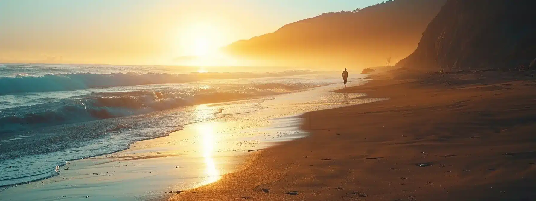 a serene beach at sunset with a solitary figure walking along the shoreline, symbolizing the journey of addiction recovery through emdr therapy.