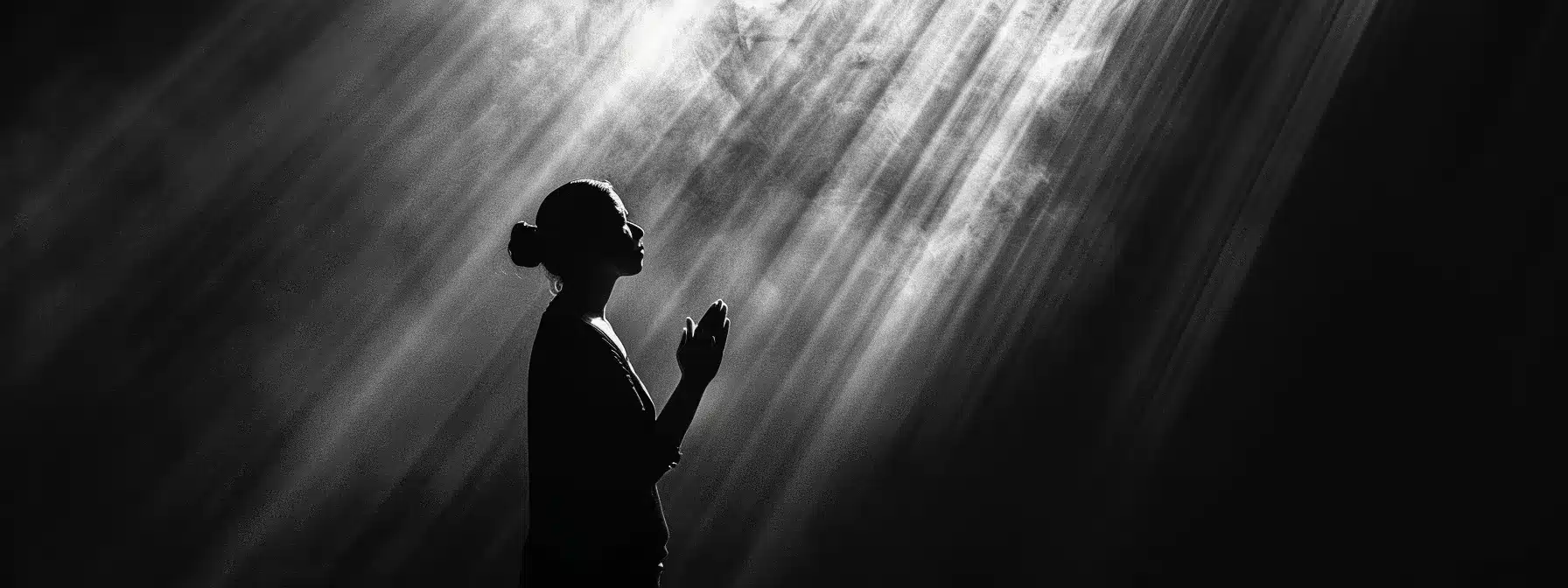 a person in silhouette standing in a beam of light, hands folded in prayer, surrounded by darkness symbolizing the power of faith in addiction recovery.