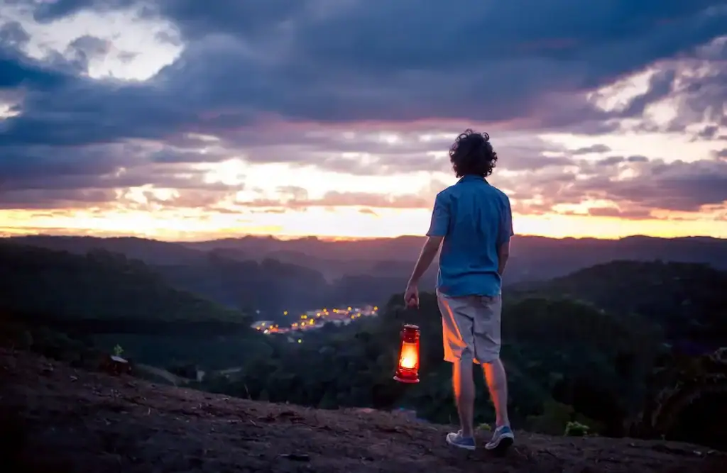 Nighttime scene at sunset with a young man holding a lantern overlooking a scenic landscape, representing hope and recovery at Firm Foundation Treatment Center for addiction and mental health support.