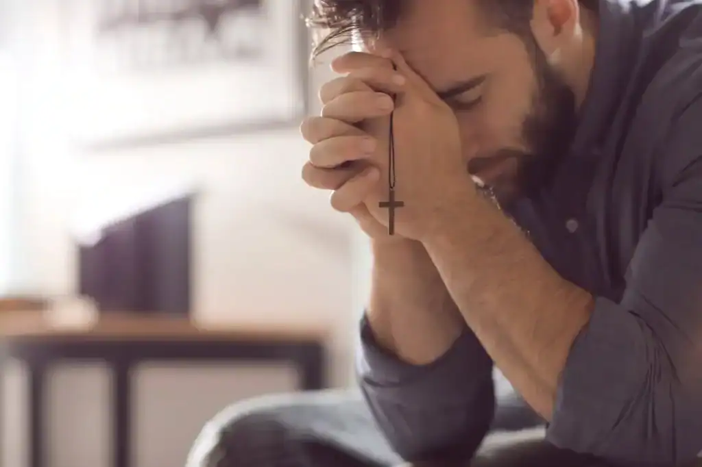 A man praying with hands clasped and a cross necklace, seeking spiritual healing and support in recovery at Firm Foundation Treatment Center.