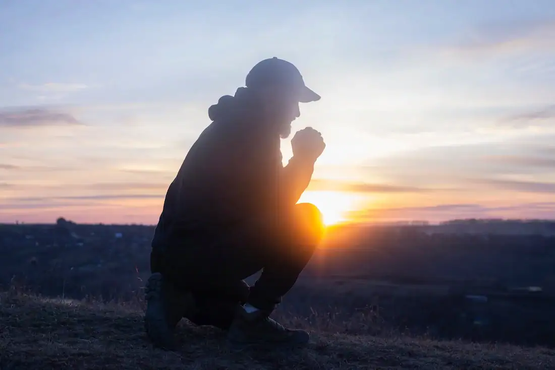 Praying man silhouette during sunrise at dawn representing hope and recovery in addiction treatment imagery.