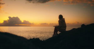 A woman sitting on rocks thinking about How a Leap of Faith Might Feel.