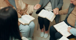 A group of people holding hands praying over a faithful friend bible verse​.