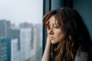 Sad woman looking out the window asking herself Can You Get Disability For Depression.